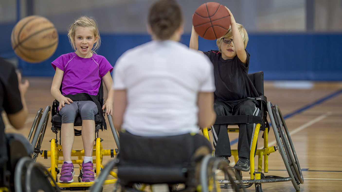 A coach and two children learning basketball. All are in wheelchairs